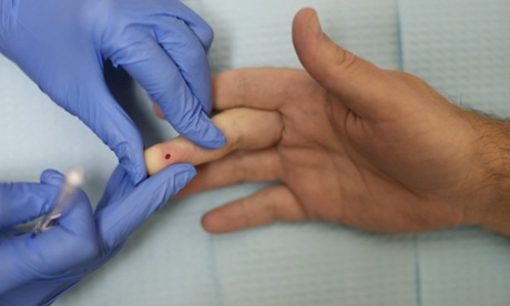 A health educator massages a drop of blood from a man's finger while conducting an HIV test.