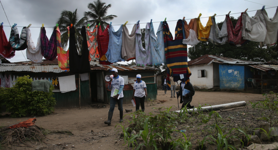 Above, UN health officials go door-to-door to speak with residents about Ebola prevention measures. The WHO says it could take another nine months to get the outbreak under control.