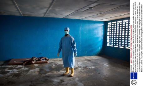 A healthcare worker stands next to a woman who has died of Ebola related symptoms in West Point, Monrovia, Liberia.