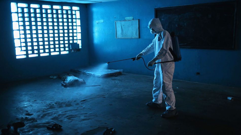 A Liberian health worker disinfects a corpse after the man died in a classroom now used as Ebola isolation ward on August 15, 2014 in Monrovia, Liberia.