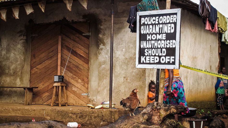 A child, center, stands underneath a signboard reading 'Police order quarantined home unauthorised should keep off' as a family home is placed under quarantine due to the Ebola virus in Port Loko, Sierra Leone, Wednesday, Oct. 22, 2014.