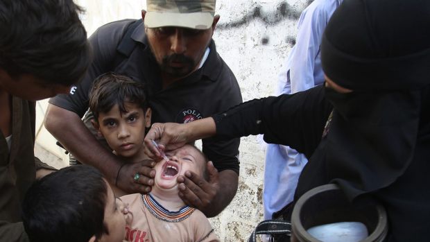 Brave work ... A Pakistani police officer helps a health worker to give polio vaccine to a child in Karachi, Pakistan.