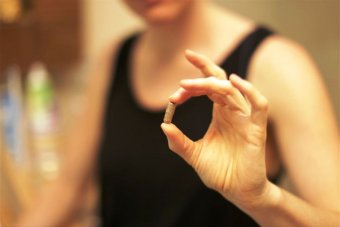 A woman holding a capsule of dehydrated placenta mixed with other herbs.