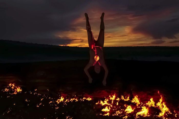 A man in a white body suit covered in lights doing a hand stand